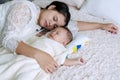 Infant asleep lying on the bed with his mother hug in the bedroom. Young mom cuddling her son sleeping together on the Royalty Free Stock Photo