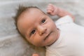 An infant baby boy with cute brown hair, laying on his back on a grey blanket with his arms raised up and looking at the Royalty Free Stock Photo