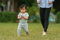 infant baby learn walking first step on grass field with mother helping in park Royalty Free Stock Photo