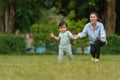 infant baby learn walking first step on grass field with mother helping in park Royalty Free Stock Photo