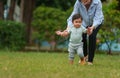 infant baby learn walking first step on grass field with mother holding hand helping in park Royalty Free Stock Photo