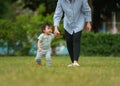 infant baby learn walking first step on grass field with mother holding hand helping in park Royalty Free Stock Photo