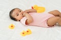 infant baby putting hands in mouth with sucking fingers and yellow rubber duck toy on bed Royalty Free Stock Photo