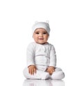 Infant baby toddler sits on the floor in white jumpsuit overall and funny hat with ears touching her legs