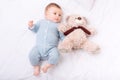 Infant boy lying in bed and grabbing teddy bear.