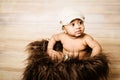 Infant dogla boy wearing hat sitting in a fluffy furry basket wooden background modern studio shoot