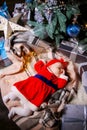 An infant dressed like a little Santa sleeping under the Christmas tree