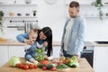 Infant girl mixing salad with metal spoons and mother& x27;s help