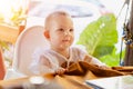 Infant girl is sitting on a baby high chair in a street cafe by the table. Children in white dress dabbles and pulls the Royalty Free Stock Photo