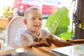 Infant girl is sitting on a baby high chair in a street cafe by the table. Children in white dress dabbles and pulls the Royalty Free Stock Photo