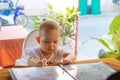 Infant girl is sitting on a baby`s high chair in a street cafe. Children reading chooses and studies the menu in the restaurant Royalty Free Stock Photo