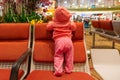 Infant girl travels. First time at the airport. Baby in living coral hoodie standing on a chair, back to the camera Royalty Free Stock Photo