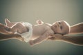 Infant held by hands of both parents on gray background.