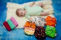 Infant laying on white, blue background near colorful textile diapers