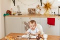 Infant little cooker boy helps to make cakes sitting at table with flour spread.