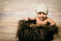 Infant mixed race healthy looking baby boy wearing knitted hat sitting in a fluffy furry basket wooden background modern studio sh