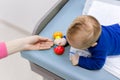 Infant with mother playing on changing table. Mom giving rattle toy to baby boy. View from above