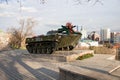 An infantry fighting vehicle stands on a pedestal decorated with flowers against the backdrop of the city on a spring day