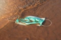 Infectious waste - medical face mask in the water on the beach sand. sea and ocean pollution since covid-19