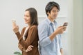 Infidelity, suspicion asian young couple love standing back to back, husband watching his wife using mobile phone, spying his Royalty Free Stock Photo