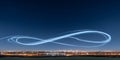 Infinity shaped light trail drawn by drones in night sky over modern cityscape skyline Royalty Free Stock Photo