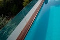 Infinity swimming pool with glassy safe fence and hardwood decking edge overlooking nature