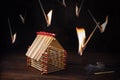 Inflamed matches are falling around a house built of matches against a dark background, insurance concept for real estate