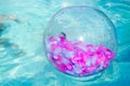 Inflatable beach ball transparent with pink feathers inside floating on the surface of the open sea pool Royalty Free Stock Photo