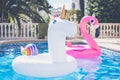 Inflatable colorful white unicorn and pink flamingo at the swim pool. Vacation time in the swimming pool with plastic