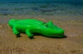 inflatable green crocodile lies on sand by sea Royalty Free Stock Photo