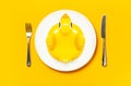 Inflatable mini yellow chicken or duckling on white plate, fork knife on yellow background. Creative food concept, tobacco chicken