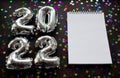 Inflatable numbers New Year 20212 on the left. Black background with shiny golden green and silver stars. White notebook, copy