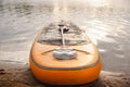 An inflatable SUP board with an orange paddle lies on the beach. Surfboard on the beach