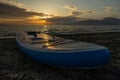 An inflatable surfboard lies on the seashore against the background of the sunset