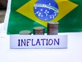 Inflation in Brazil concept. Handwritten Inflation on a paper board, growing up arrow, coins and Brazilian flag in the background