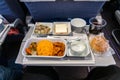 Inflight airplane Asian food set meal served consisting rice and spicy chicken, appetizer, dessert, bun and red wine Royalty Free Stock Photo