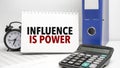 influence is power words on white notebook and calculator, black vintage alarm clock and blue paper folder