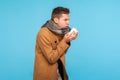 Influenza season. Portrait of flu-sick man in autumn coat and scarf sneezing in napkin, feeling unwell Royalty Free Stock Photo