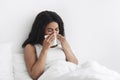 Influenza. Sick african american woman blowing runny nose sneezing, sitting in bed, copy space Royalty Free Stock Photo