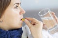 Influenza treatment or coronavirus . Flu-sick woman, wrapped in warm scarf and blanket , taking pills holding glass of water Royalty Free Stock Photo