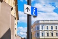 Info sign with a forward/up arrow on a street pole, with city architecture in the back