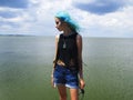 An informal girl in a black top with green hair stands in the wind