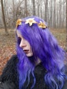 An informal goth girl with purple hair and a golden crown with flowers walks in a foggy forest. Forest Nymph.