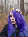 An informal goth girl with purple hair and a golden crown with flowers walks in a foggy forest. Forest Nymph.