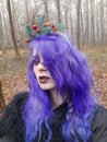 An informal goth girl with purple hair and a New Year`s wreath with fir branches walks in a foggy forest