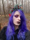 An informal goth girl with purple hair and a New Year`s wreath with fir branches walks in a foggy forest