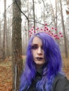 An informal goth girl with purple hair and a pink crown with berries walks in a foggy forest. Forest Nymph.