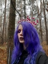 An informal goth girl with purple hair and a pink crown with berries walks in a foggy forest. Forest Nymph.