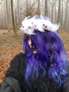 An informal goth girl with purple hair and a white wreath with feathers walks in a foggy forest. Forest Nymph. Spirit of the fores