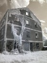 Infrared surreal landscape with snowy trees, reflections of clouds and trees in the water, stone house, photographed with a Royalty Free Stock Photo